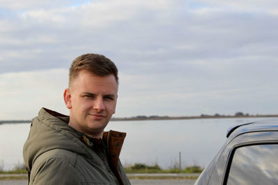 Portrait of man standing by car against sky