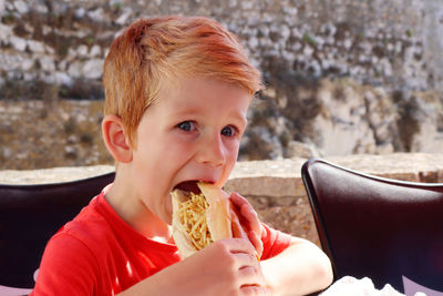 A boy opens his mouth and takes a bite of a stuffed bun.a boy eating street food at a summer café.  