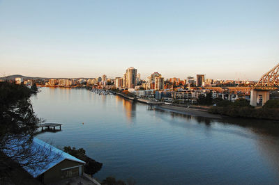 Buildings by river against clear sky in city