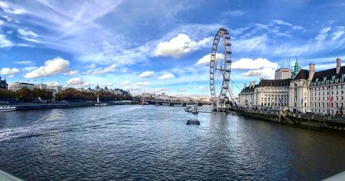 View of buildings by river against cloudy sky