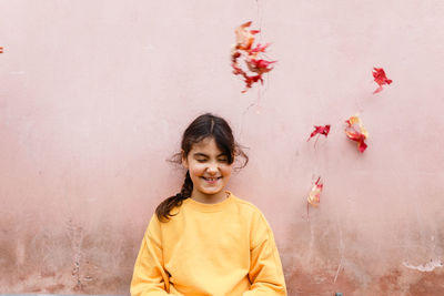 Smiling girl in yellow top stands under falling red leaves