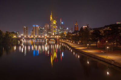 Illuminated buildings by river against sky at night