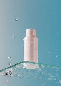 White tube of cosmetic product on a glass shelf and falling drops on a blue background. skin care