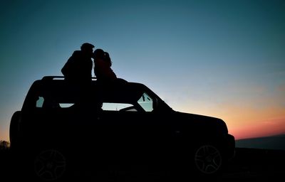 Silhouette people on car against sky during sunset