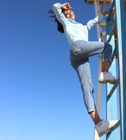 Low angle view of woman on ladder against blue sky