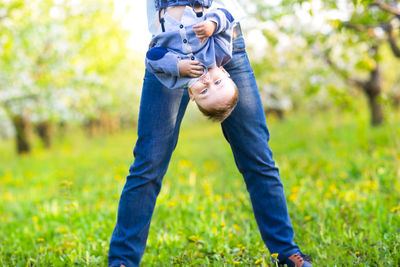 Low section of mother holding baby upside down at park