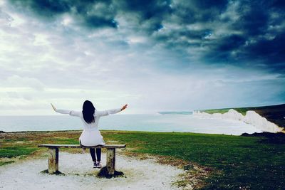 Rear view of woman standing at beach against sky