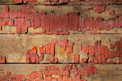 Full frame shot of weathered wooden planks with leftovers of peeled off red paint under sunlight