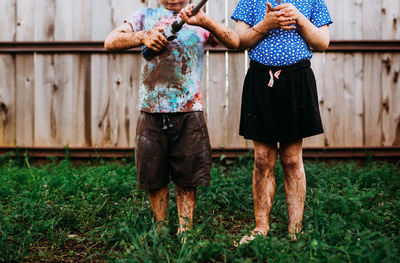 Young brother and sister standing outside covered in mud