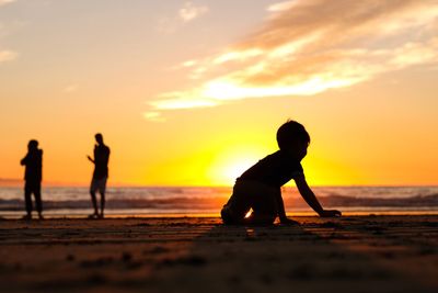 Silhouette children on beach against sky during sunset