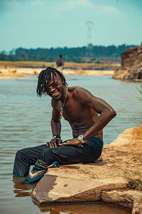 Full length of shirtless man sitting on rock