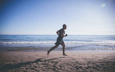 Side view of man running at beach against sky