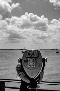 Close-up of girl holding coin-operated binoculars by sea against sky