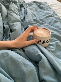 High angle view of woman holding coffee cup on bed