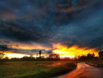Road passing through field against cloudy sky