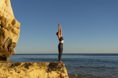 Fit female practicing yoga on a rock by the sea.