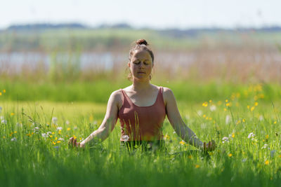 Woman meditating in high grass outdoors in summer near lake