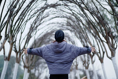 Rear view of woman with arms outstretched standing against trees