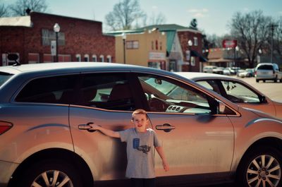 Portrait of boy standing against car in city