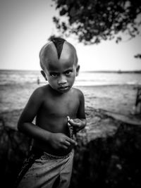 Portrait of shirtless boy standing on beach against sky