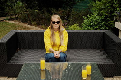 Portrait of smiling young woman wearing sunglasses sitting on sofa against plants