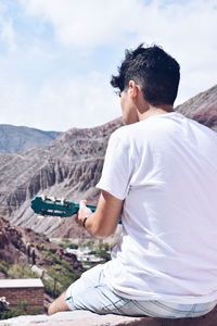 Rear view of man sitting on mountain against sky