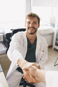 Portrait of smiling young male doctor shaking hands with nurse at office in hospital