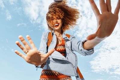 Young woman with arms raised standing against sky