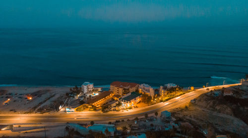 High angle view of illuminated city by sea at night