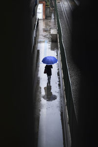 Rear view of woman walking with umbrella on railroad station platform during night