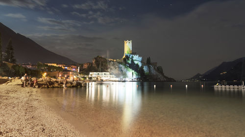 Illuminated city by lake against sky at night