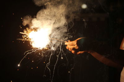 Midsection of person holding illuminated sparklers at night