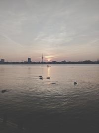 Distant view of man on boat in sea against sky during sunset