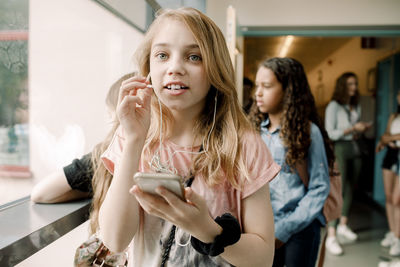 Female student talking through in-ear headphones in school corridor