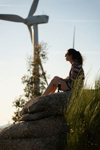 Caucasian woman on top of a boulder looking at wind turbines in fafe, portugal