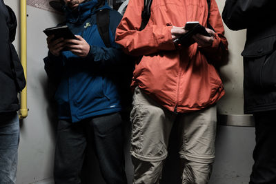 Midsection of men using mobile phones while standing in train