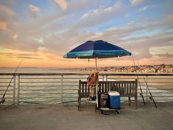 Chair on beach against sky during sunset