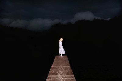 Woman standing on pier over lake at night