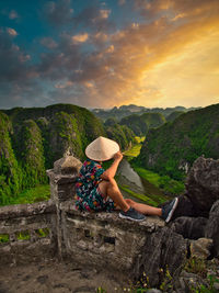 Woman sitting on land against mountain range against sky