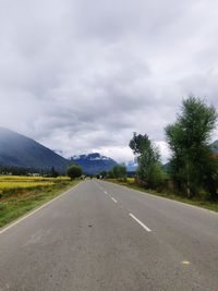 Empty road along trees and against sky