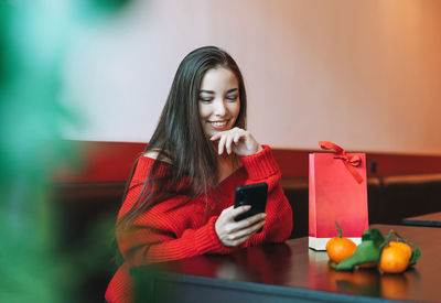 Beautiful asian woman in red clothes using mobile with gift bag in cafe, chinese new year