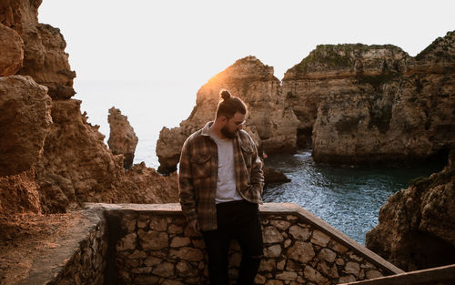 Young man standing on ledge agaisnt sunrise between rock formation in sea