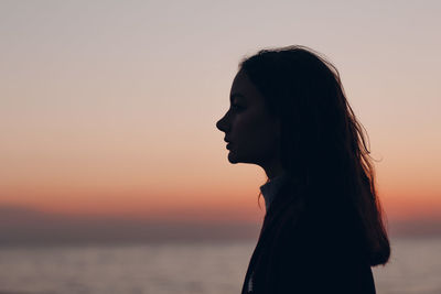 Portrait of young woman looking away against sky during sunset