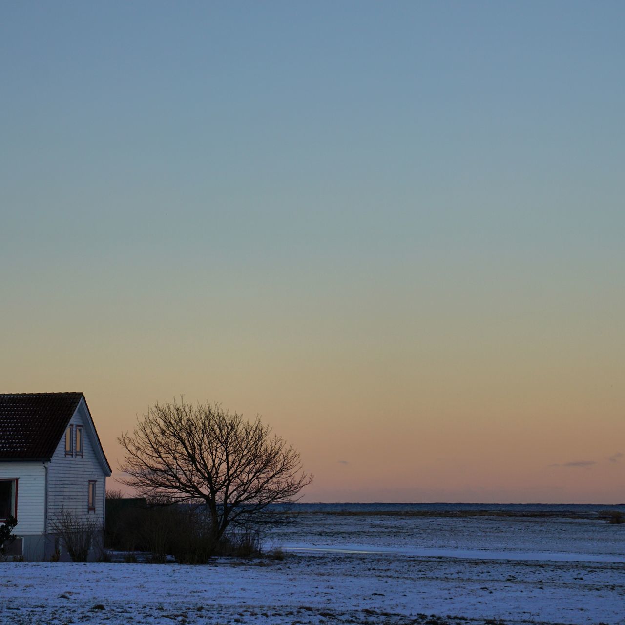 clear sky, sunset, copy space, sea, built structure, building exterior, architecture, tranquil scene, water, scenics, horizon over water, tranquility, beauty in nature, orange color, nature, tree, house, winter, cold temperature, bare tree