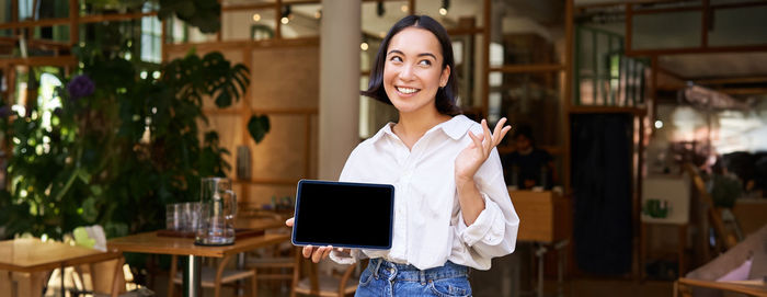 Portrait of young woman using digital tablet while standing in cafe