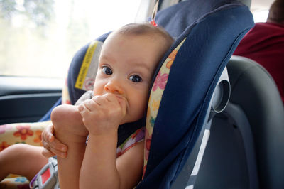 Portrait of baby girl biting foot while sitting on car seat