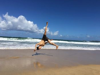 Full length of man jumping on beach against sky