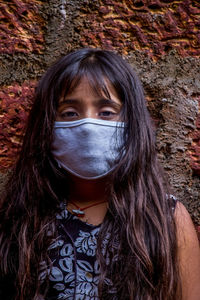 Portrait of girl wearing mask standing by wall outdoors