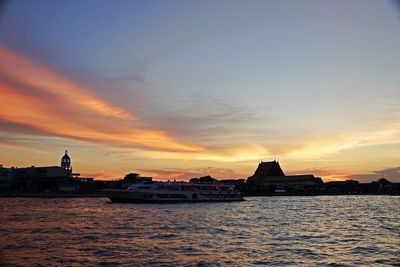 Sea by buildings against sky during sunset