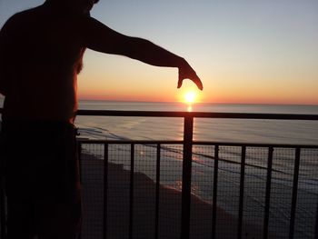 Silhouette man standing by railing against sea during sunset